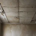 Старый, запущенный потолок с глубокими, потрескавшимися рустами (швами) между плитами, демонстрирующий необходимость их заделки и последствия игнорирования.