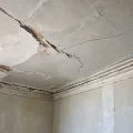 Крупный план старого, потрескавшегося потолка с облупившейся побелкой, демонстрирующий необходимость ее удаления перед ремонтом. Видны повреждения и отслаивающиеся слои старой побелки.