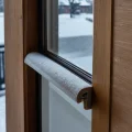Фотореалистичное изображение балконной двери, сквозь щели которой пробивается холодный воздух, демонстрируя причину сквозняков и обледенение рамы.