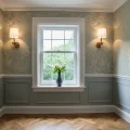 Комната в классическом стиле с зелеными обоями, бра, деревянным полом и белыми панелями. Идеи для создания изысканного интерьера.