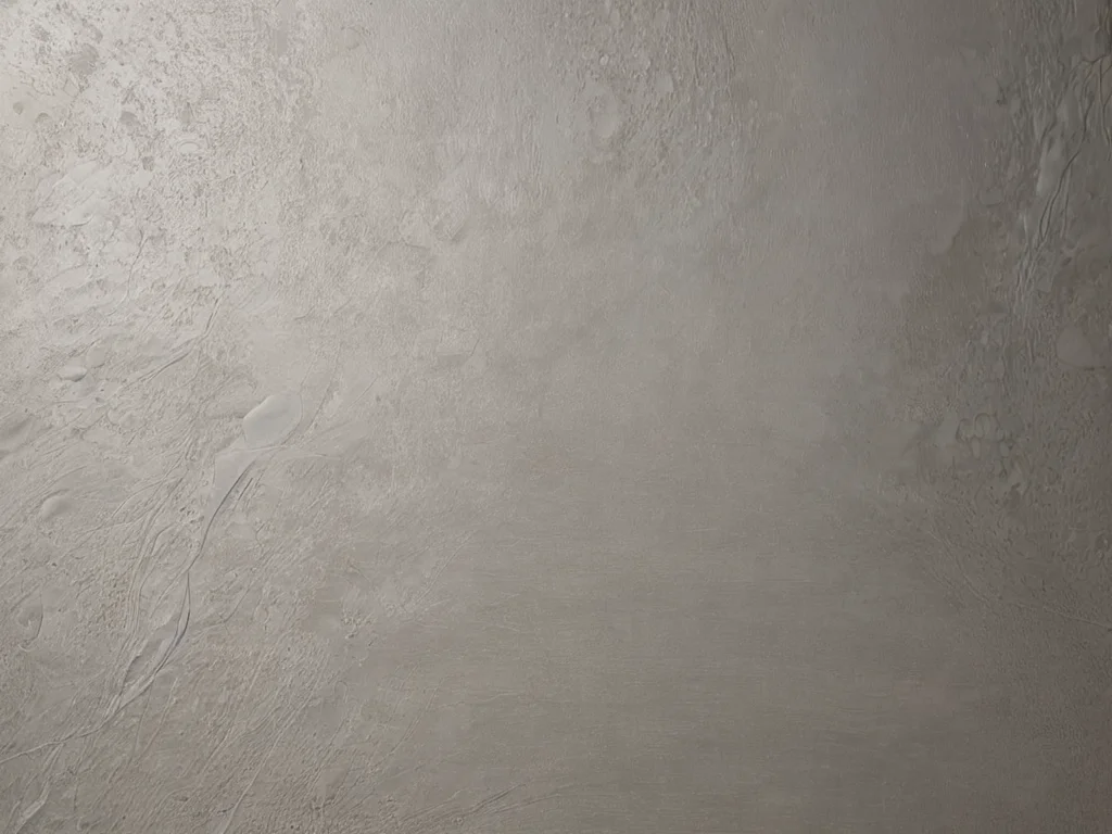 Крупный план жидких обоев с матовой поверхностью, демонстрирующих незначительные изъяны после влажной чистки, на нейтральной серой стене.