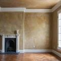 Просторная комната с камином, декоративная штукатурка на стенах, бежево-коричневая цветовая гамма, большое окно, классический стиль.